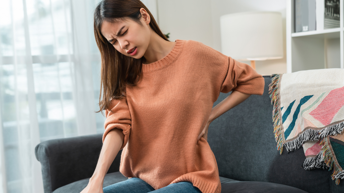 Woman on couch clutches back, showing pain.