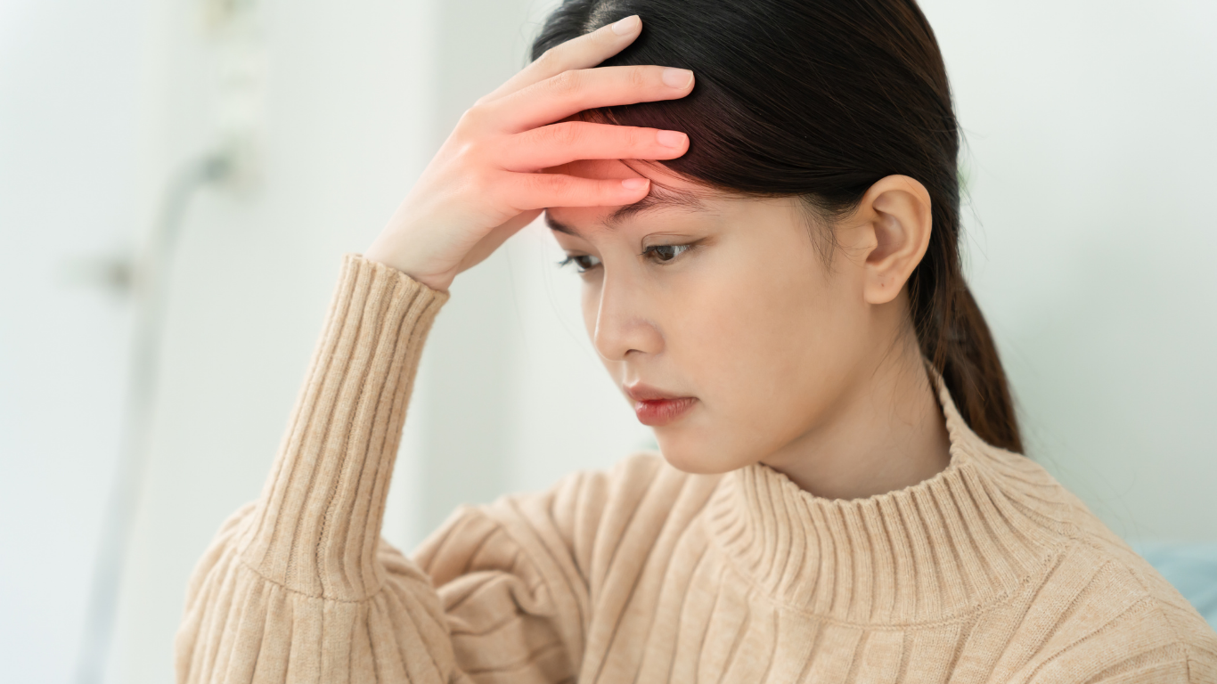 Woman with headache, hand on forehead, red highlight, neutral setting, wearing sweater.