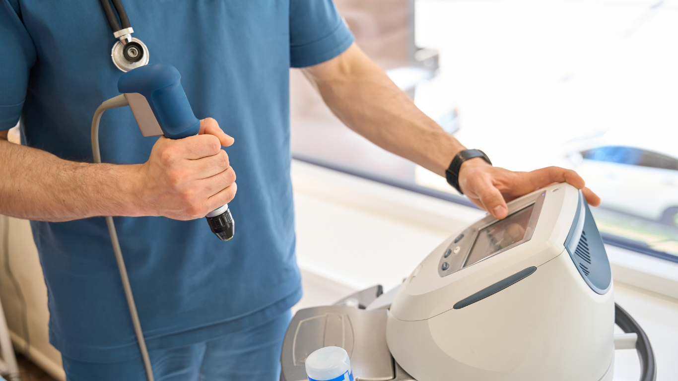 Person in blue scrubs holding a medical device, adjusting the control panel near a window.