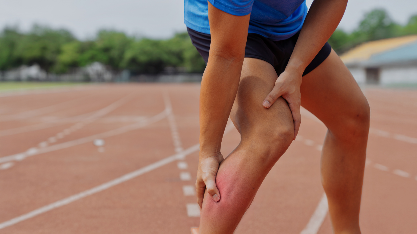 Runner holding leg on a track, showing apparent muscle strain and redness.