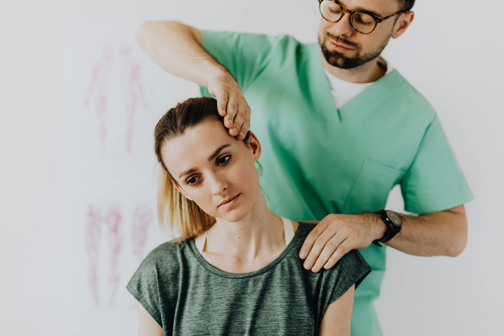 Chiropractor adjusting a person's neck. The person is looking down with a neutral expression, and the practitioner wears scrubs.
