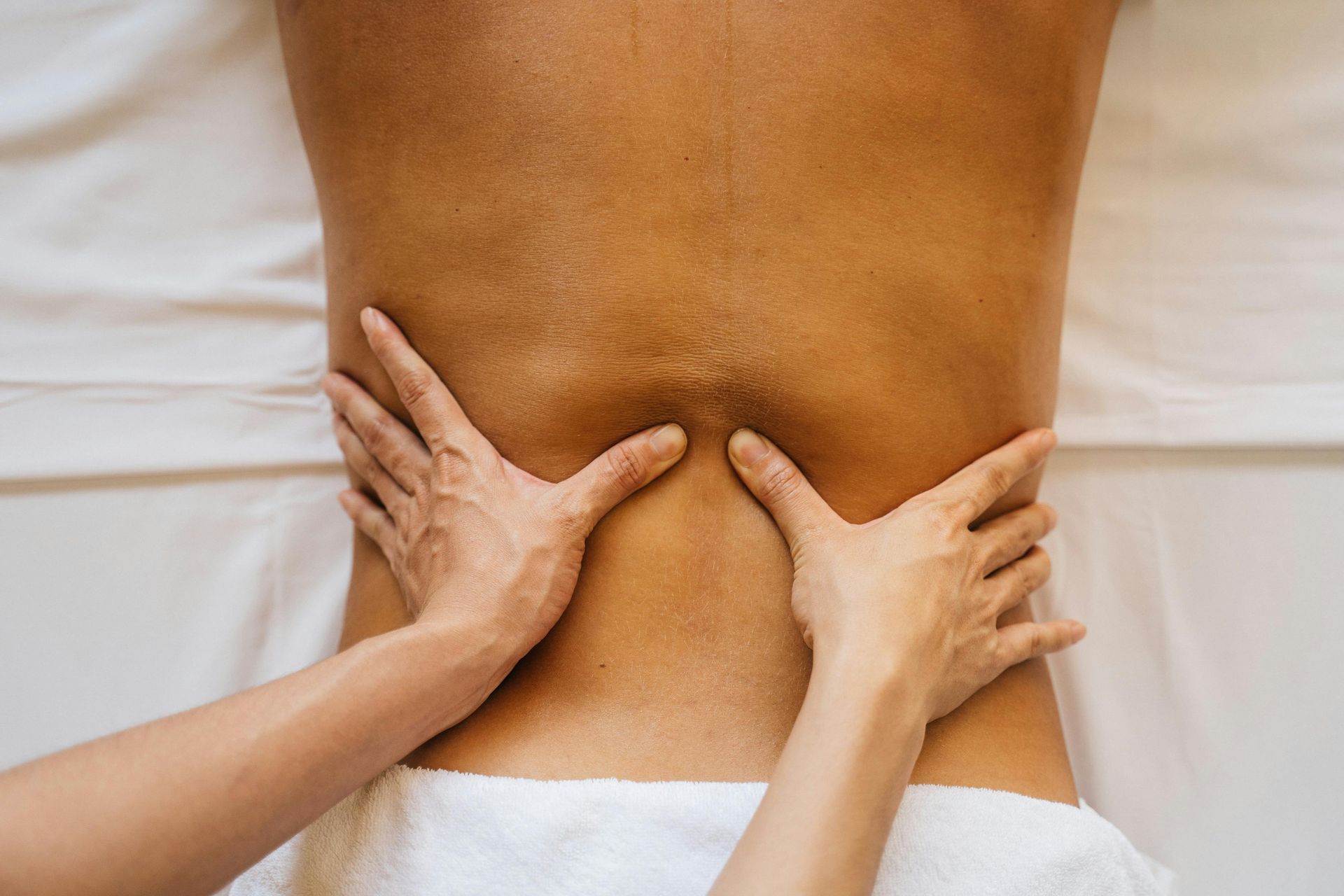 Hands pressing on a person’s lower back, suggesting massage or pain relief