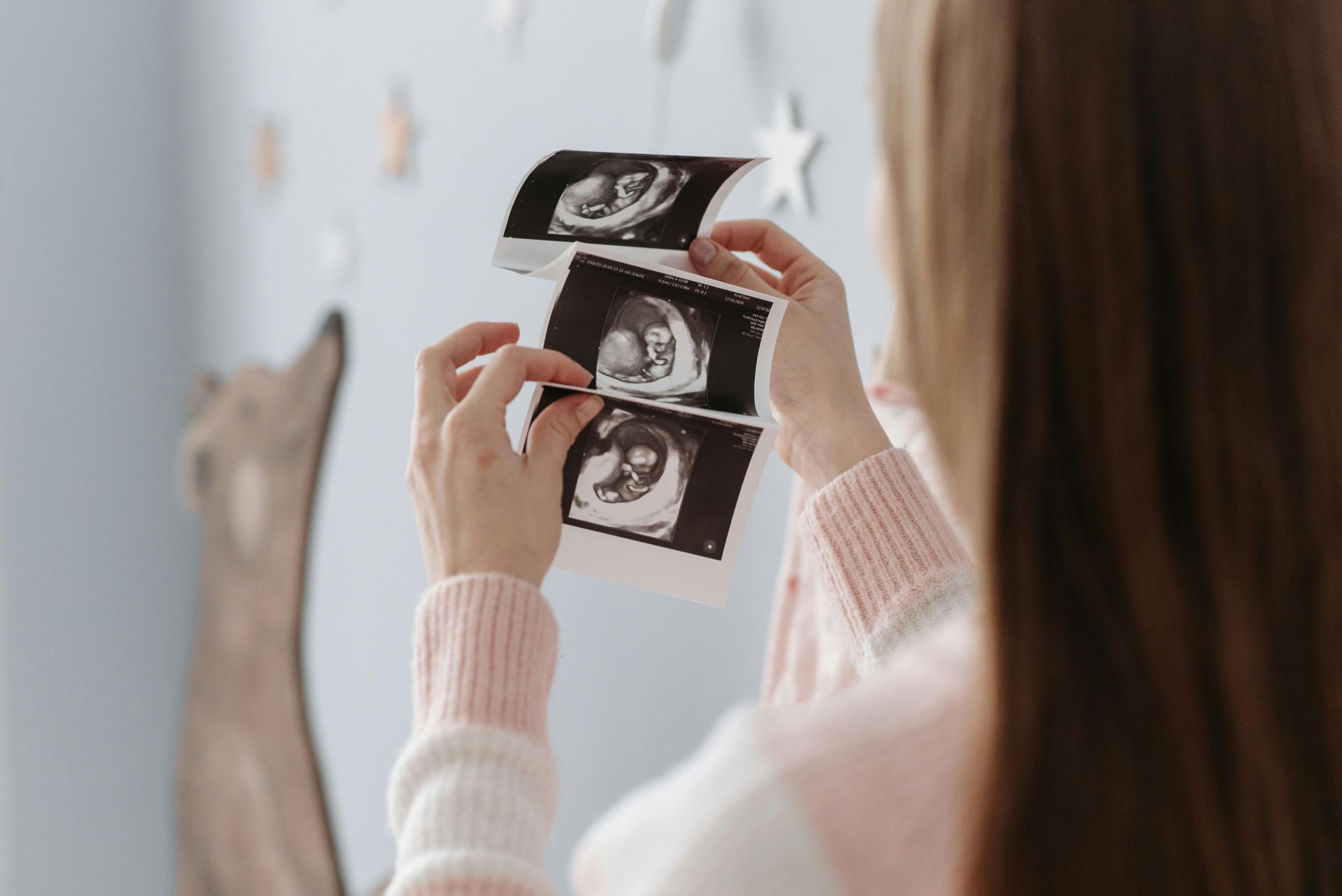 Woman holding up sonogram photos in front of a blue wall with star decorations.