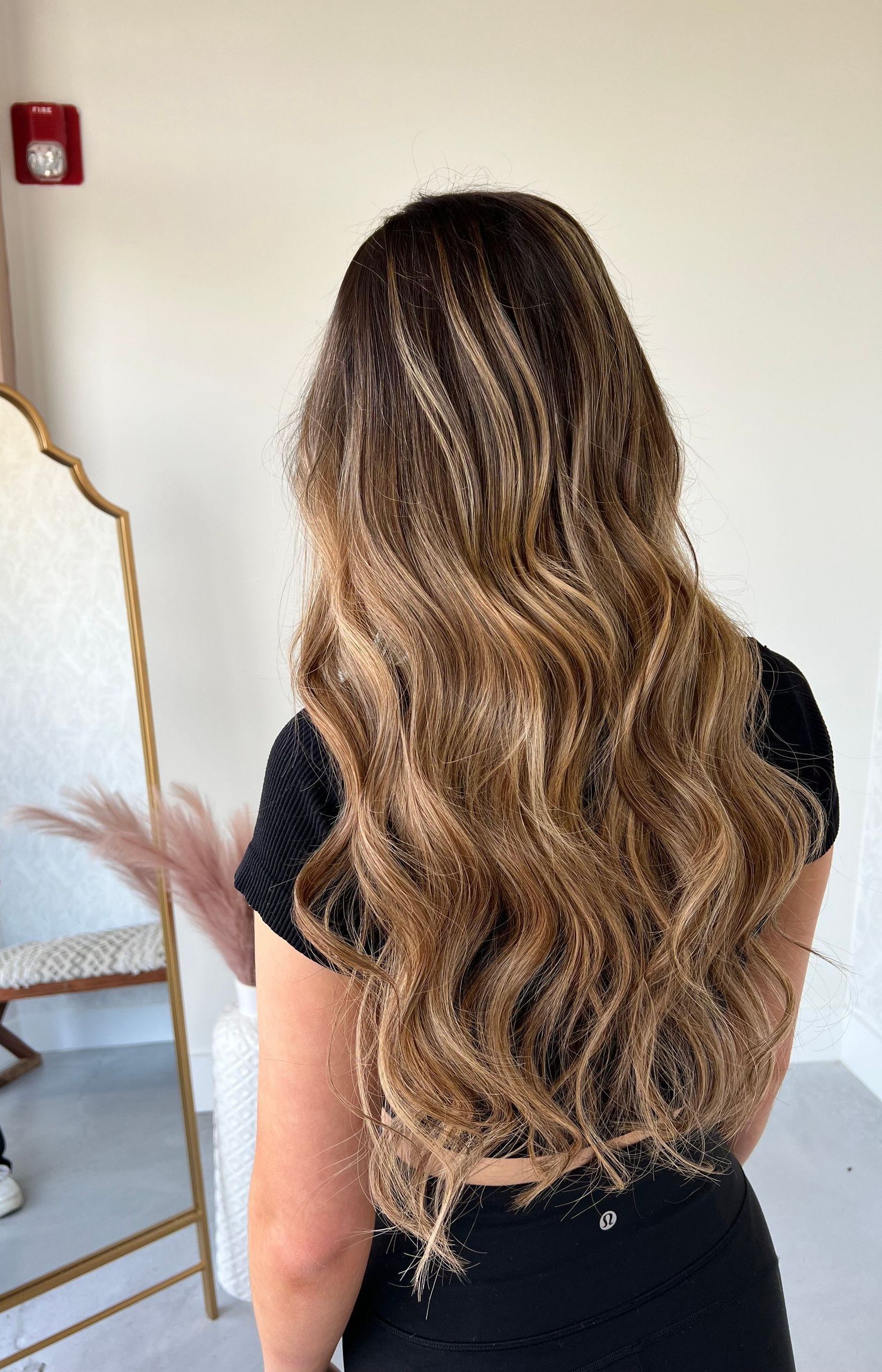 A woman with long wavy hair is standing in front of a mirror.