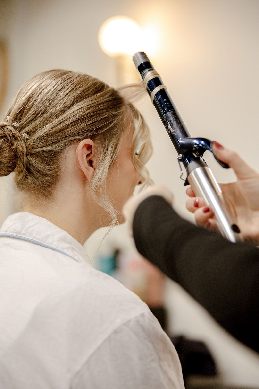 A woman is getting her hair done by a hairdresser with a curling iron.
