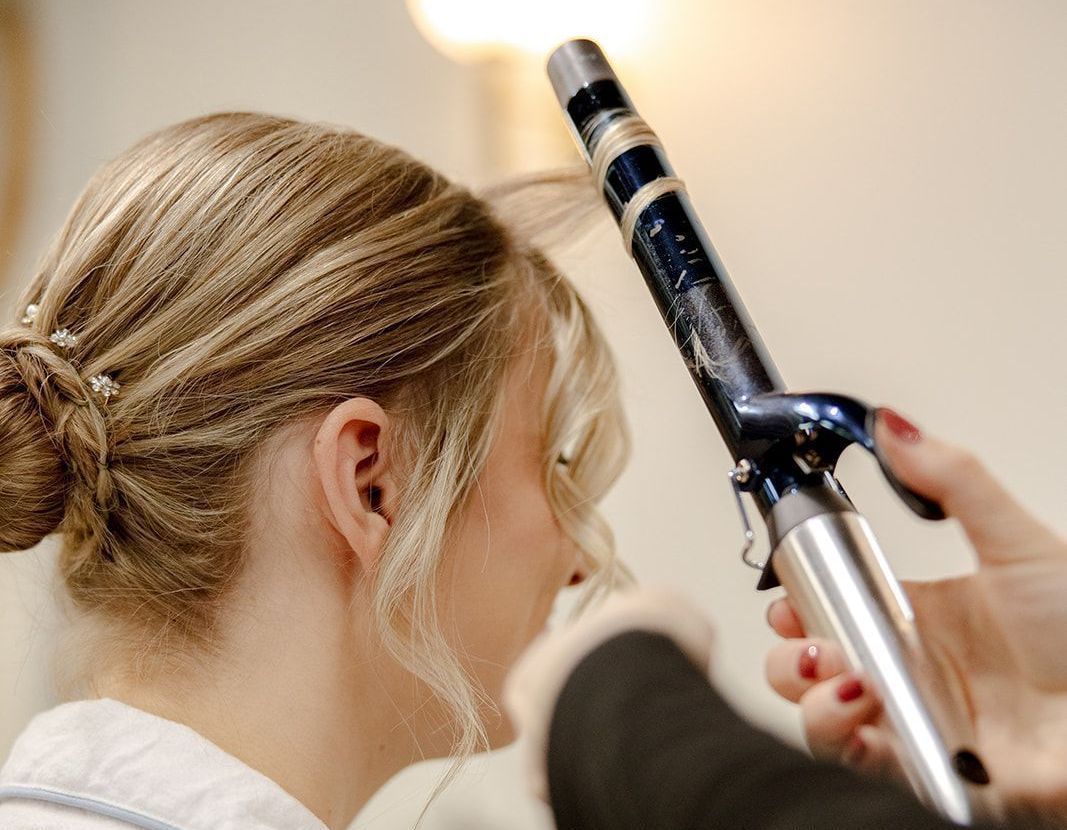 A woman is getting her hair done with a curling iron