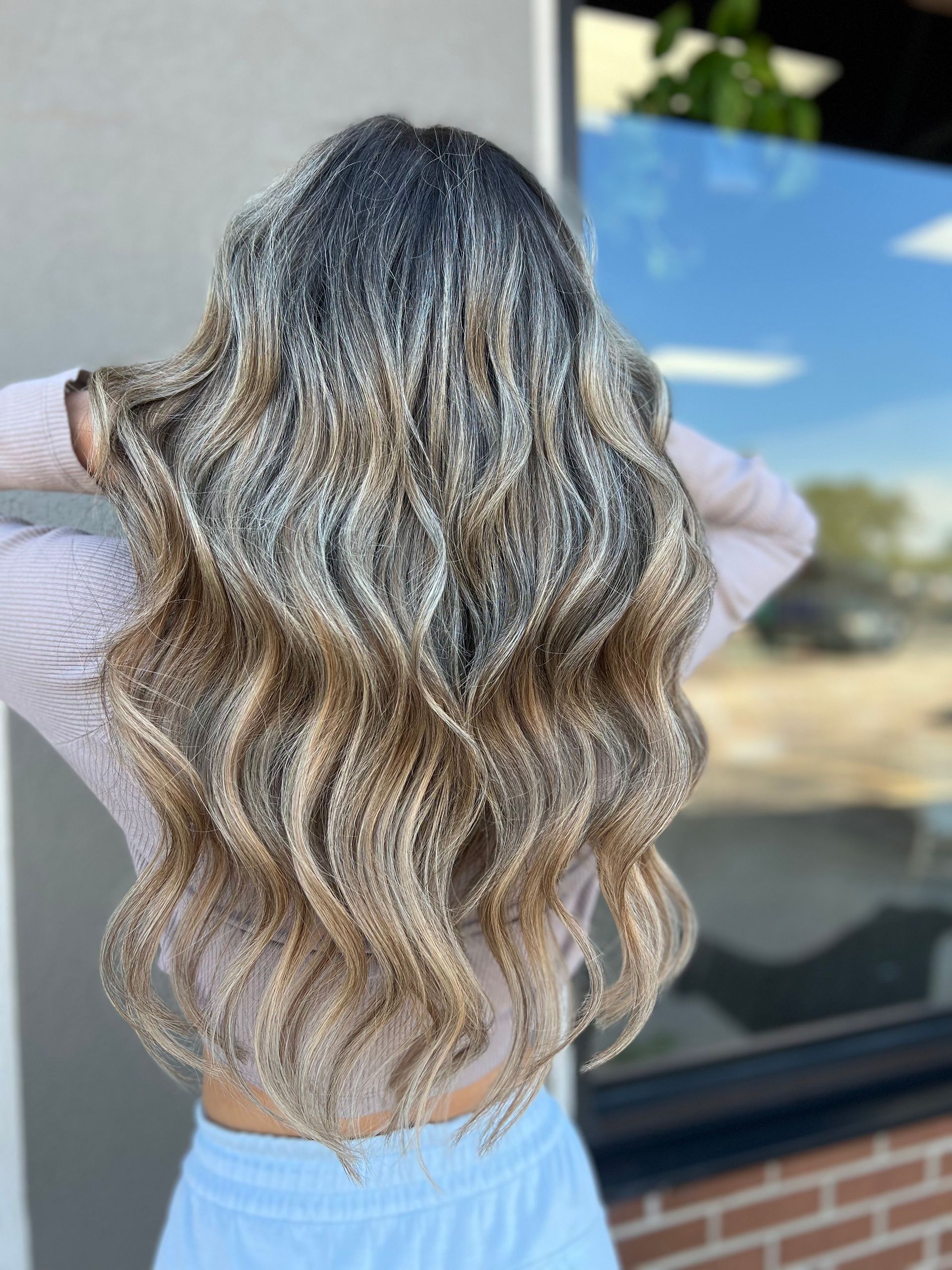 A woman with long wavy blonde hair is standing in front of a window.