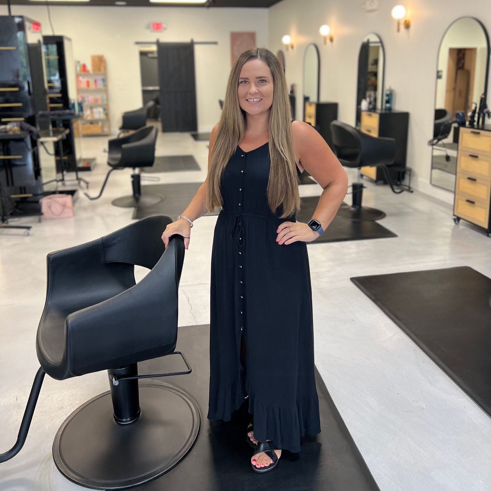 A woman in a black dress is standing next to a chair in a salon