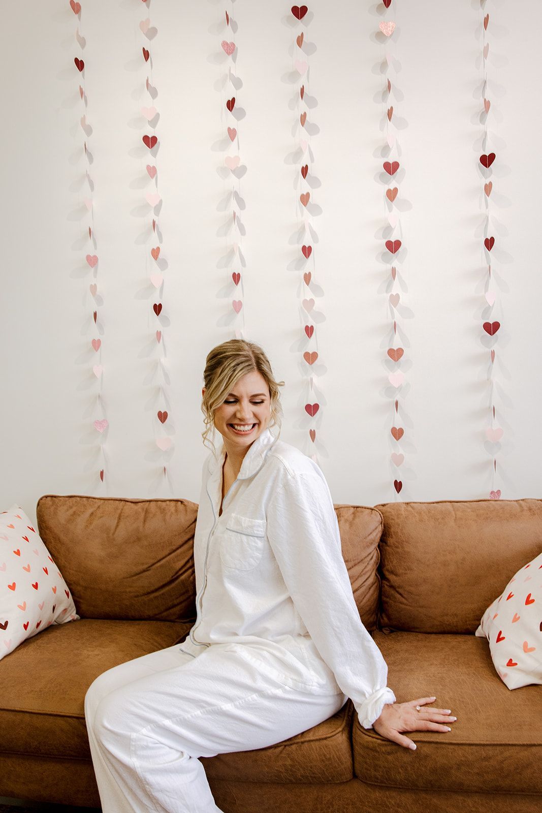 A woman is sitting on a couch in front of a wall with hearts on it.