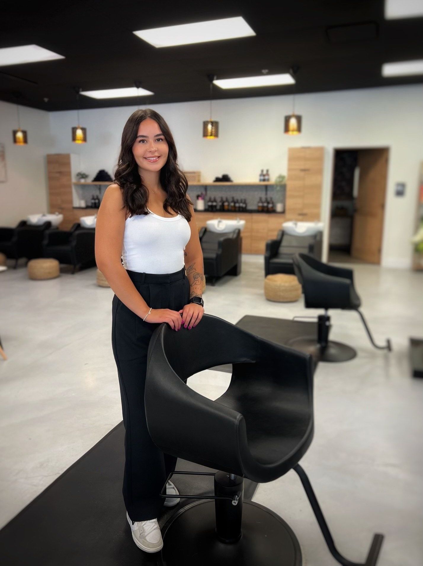 A woman is standing next to a black chair in a salon.
