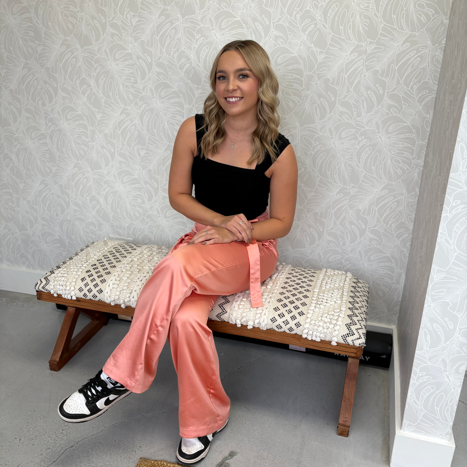 A woman in a black top and pink pants is sitting on a bench