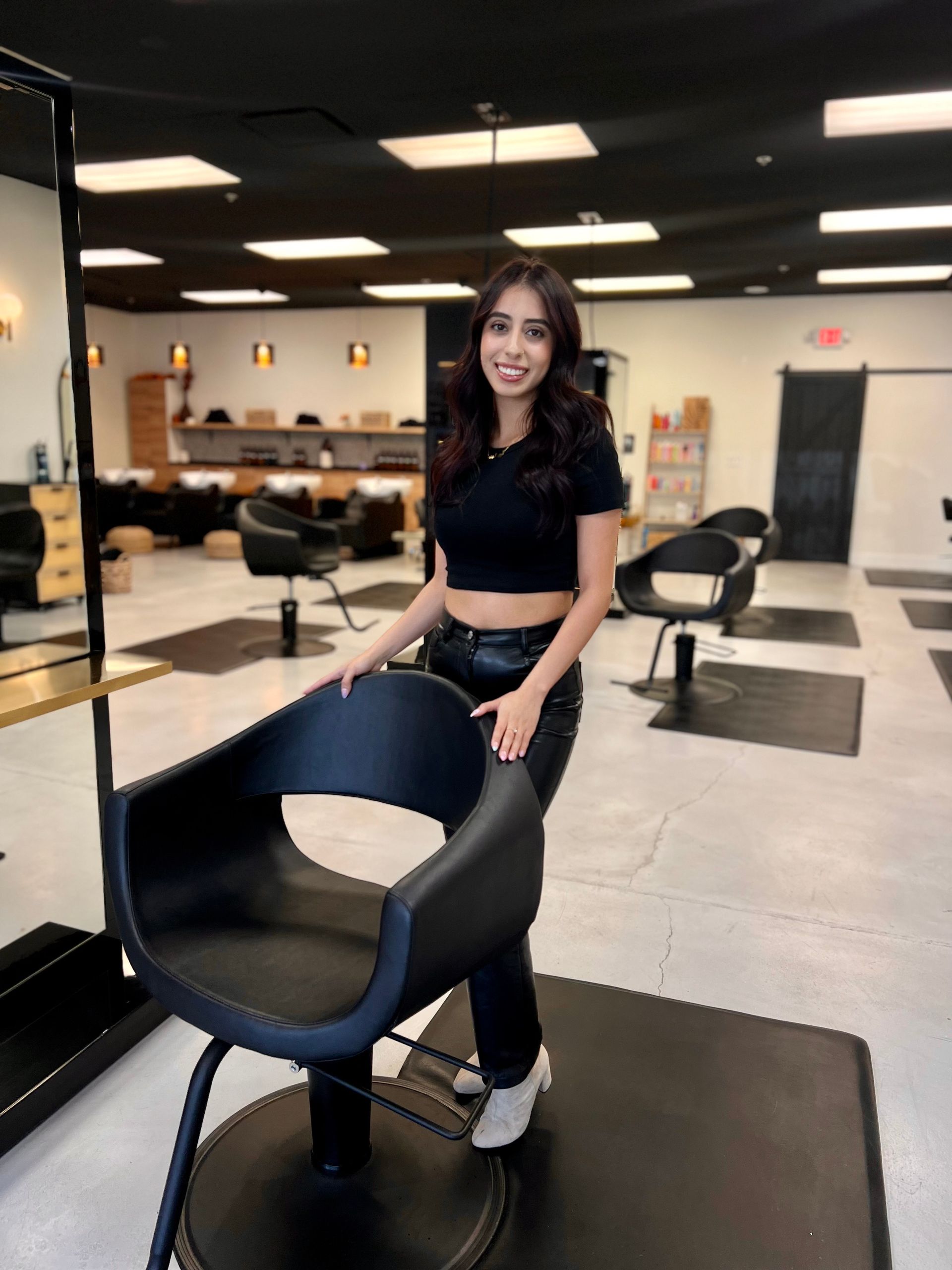 A woman is standing next to a black chair in a salon.