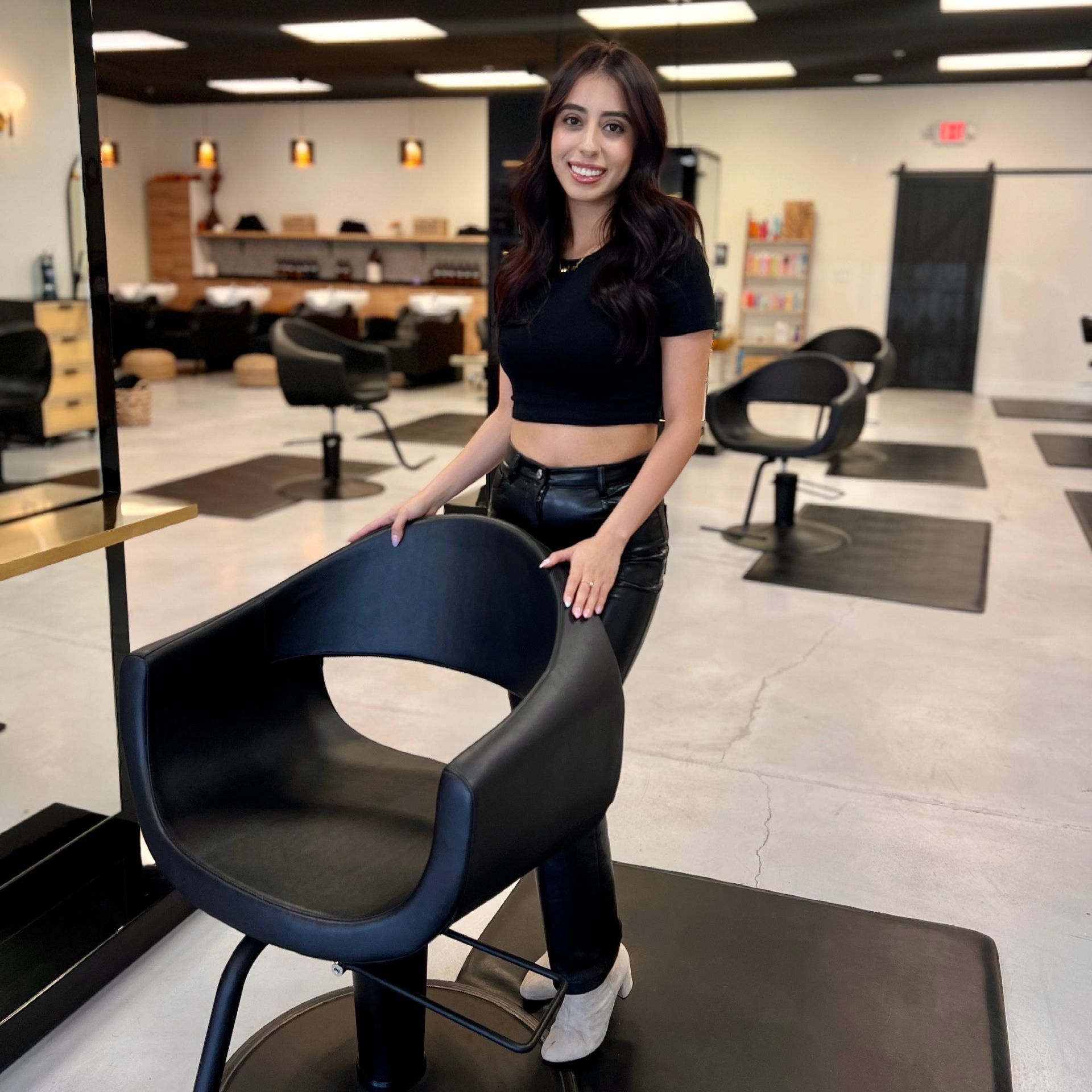 A woman is standing next to a black chair in a salon.