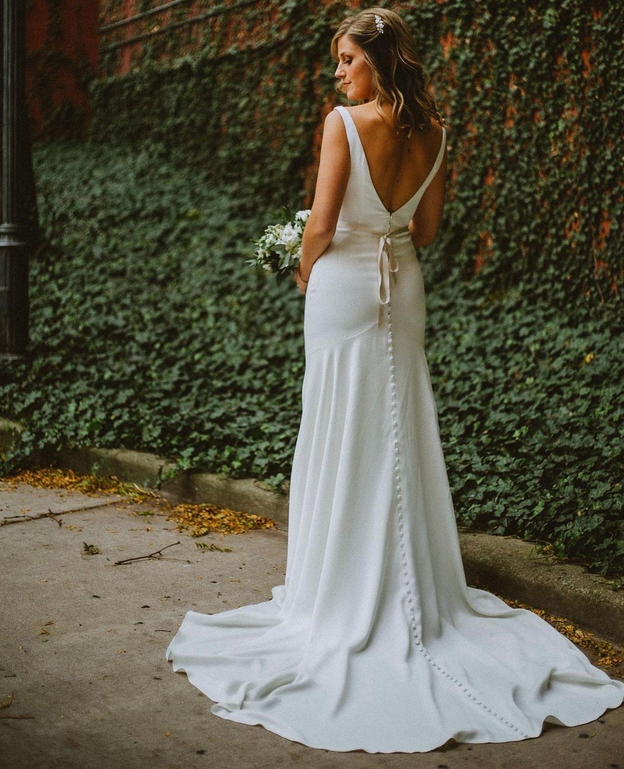 A woman in a white wedding dress is standing on a sidewalk holding a bouquet of flowers.