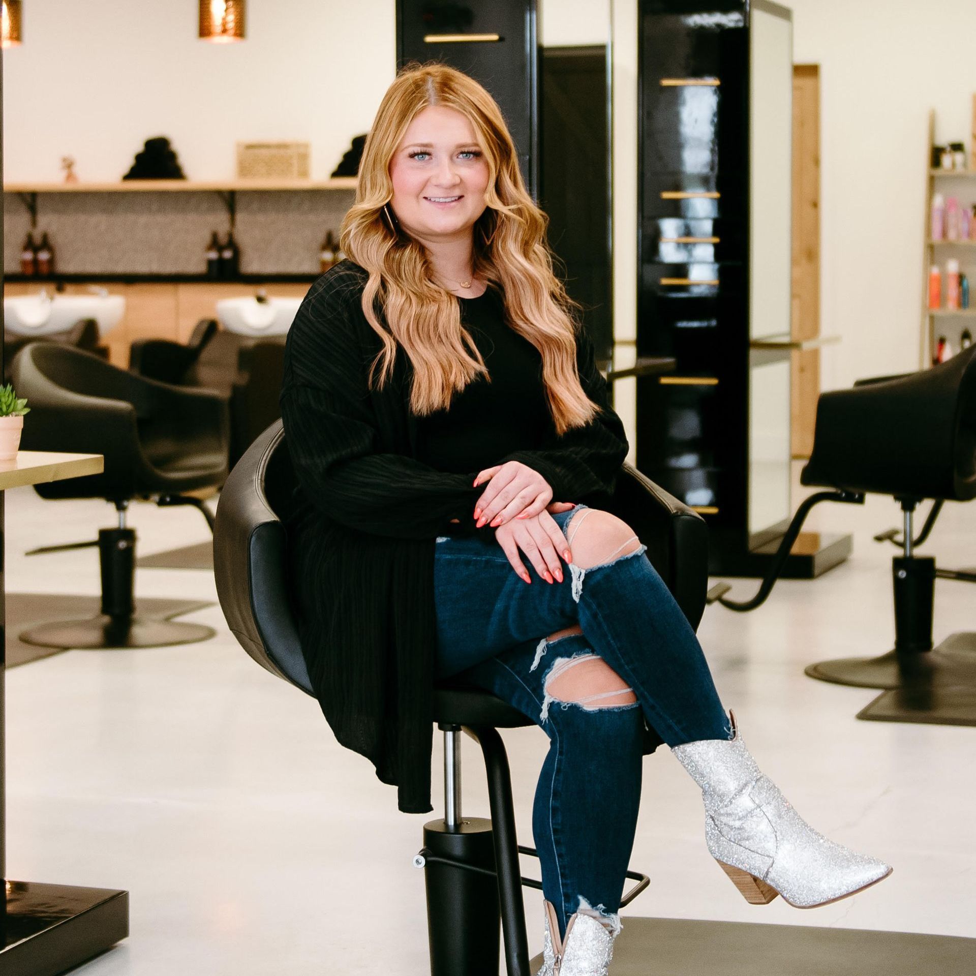 A woman in a black jacket and jeans is standing in a salon.