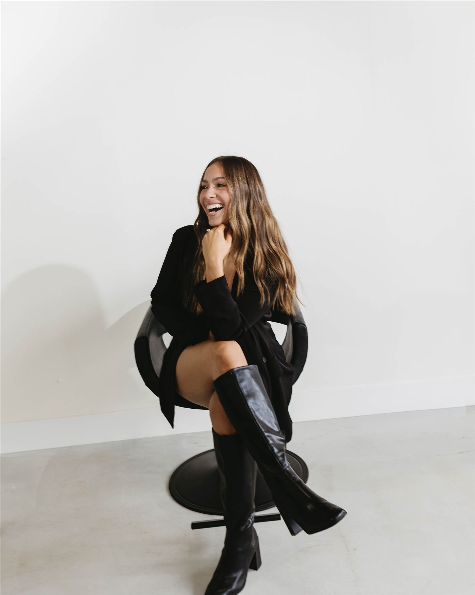 A woman in a black tank top is smiling in front of a white wall.