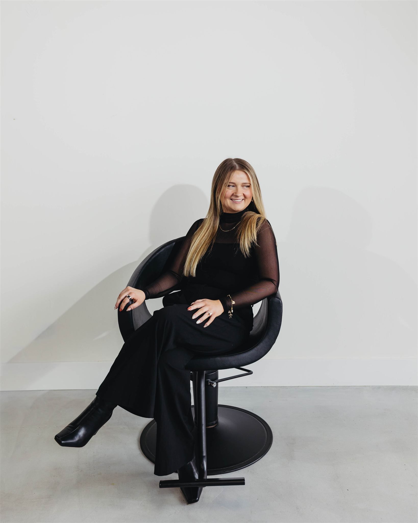 A woman in a black jacket and jeans is standing next to a chair in a salon.