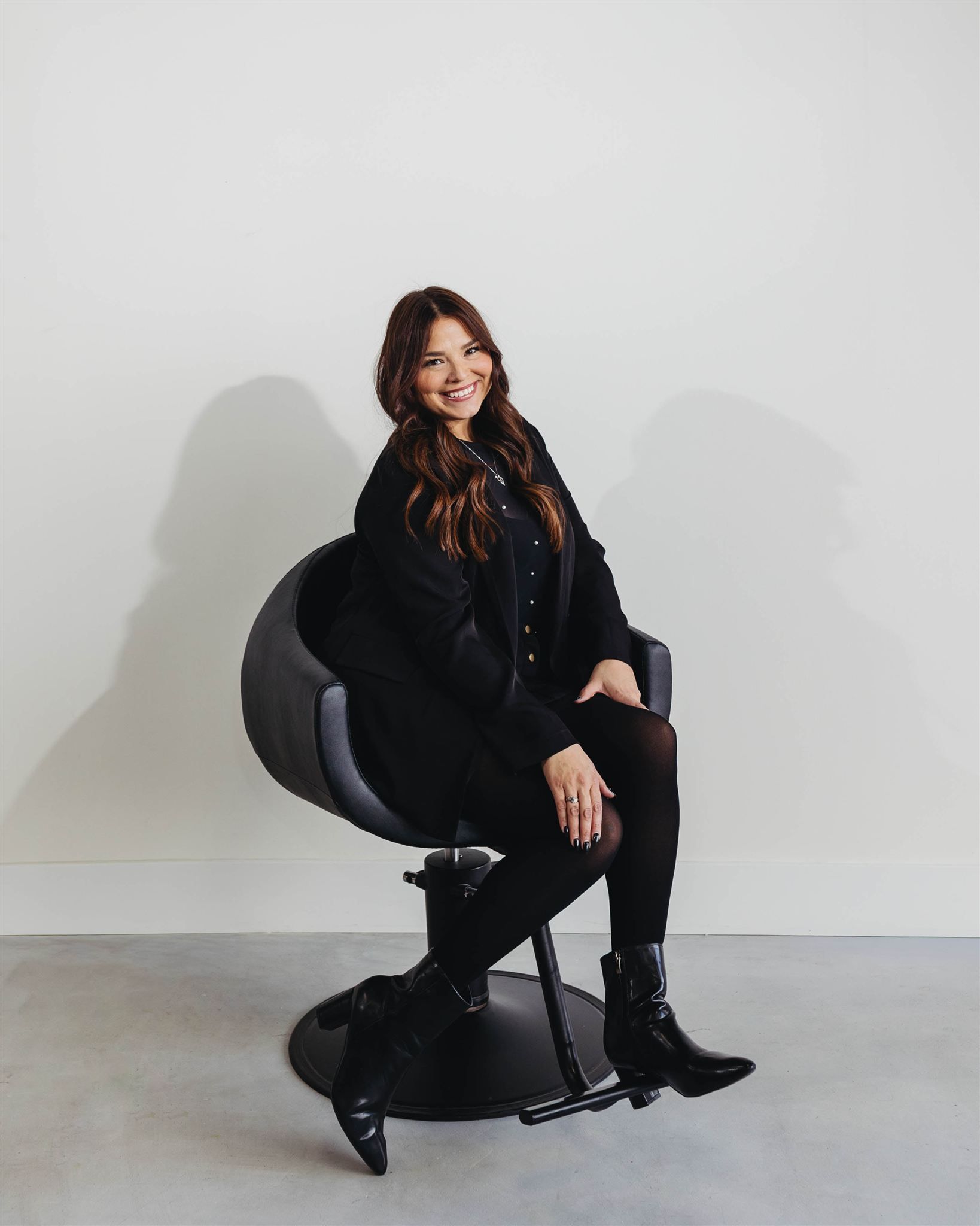 A woman in a black dress is sitting in a black chair in a salon.