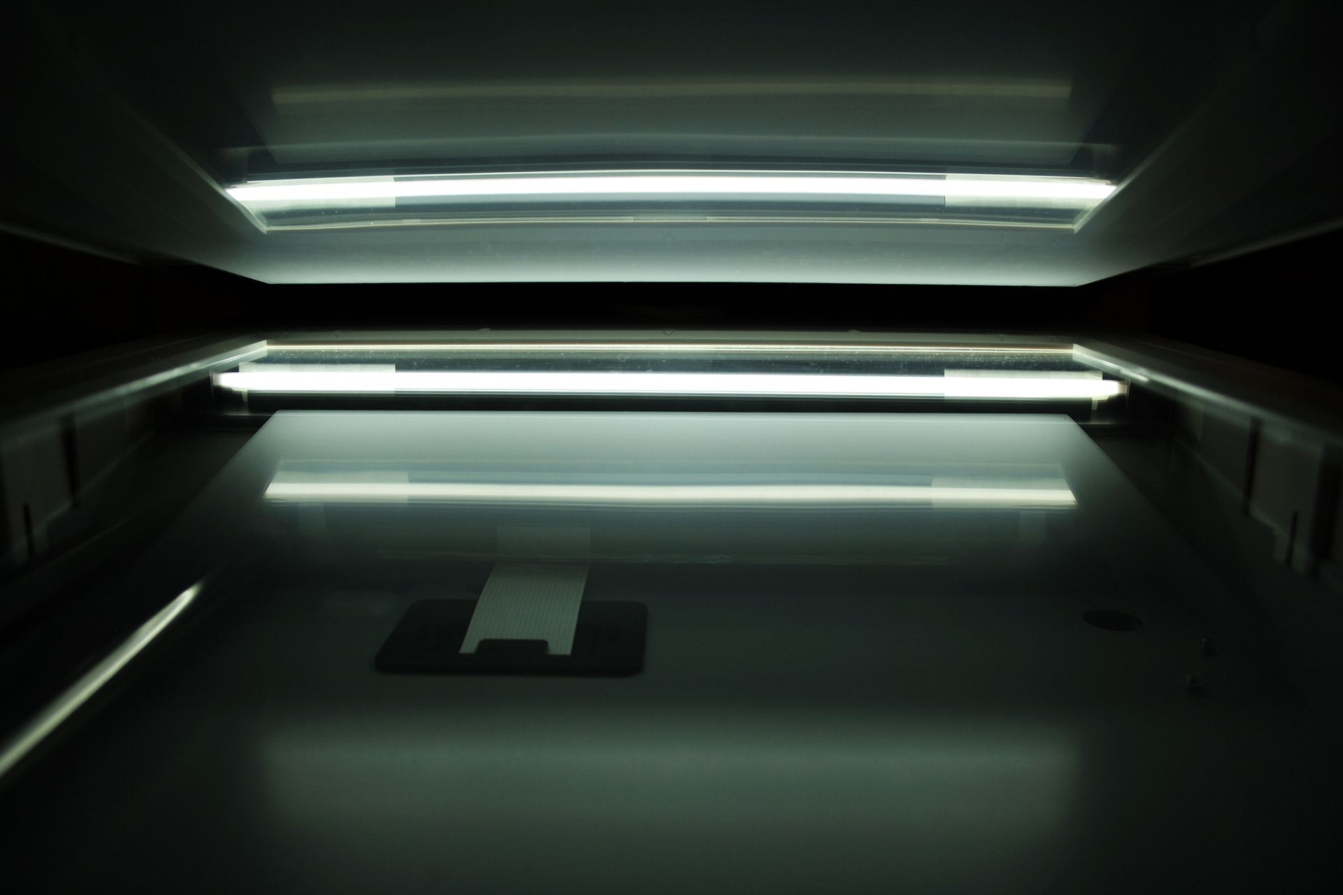Inside of a document scanner with two fluorescent lights reflecting off the glass.