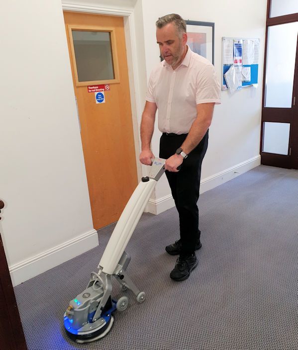 A man is using a machine to clean a carpet in a hallway