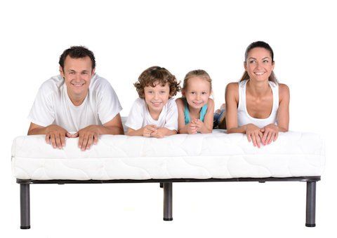 A family is laying on a mattress together and smiling.