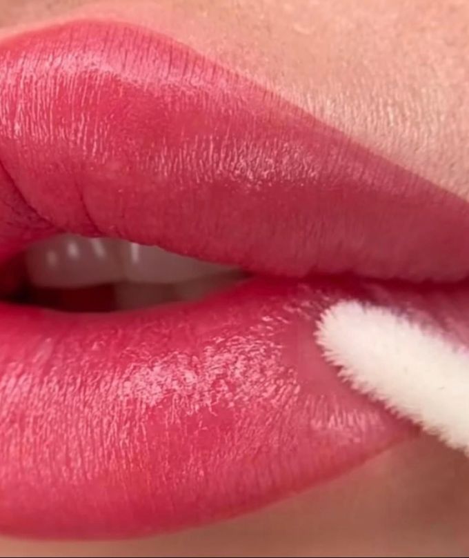 Primo piano di labbra rosa toccate con un batuffolo di cotone, probabilmente per applicare il rossetto.