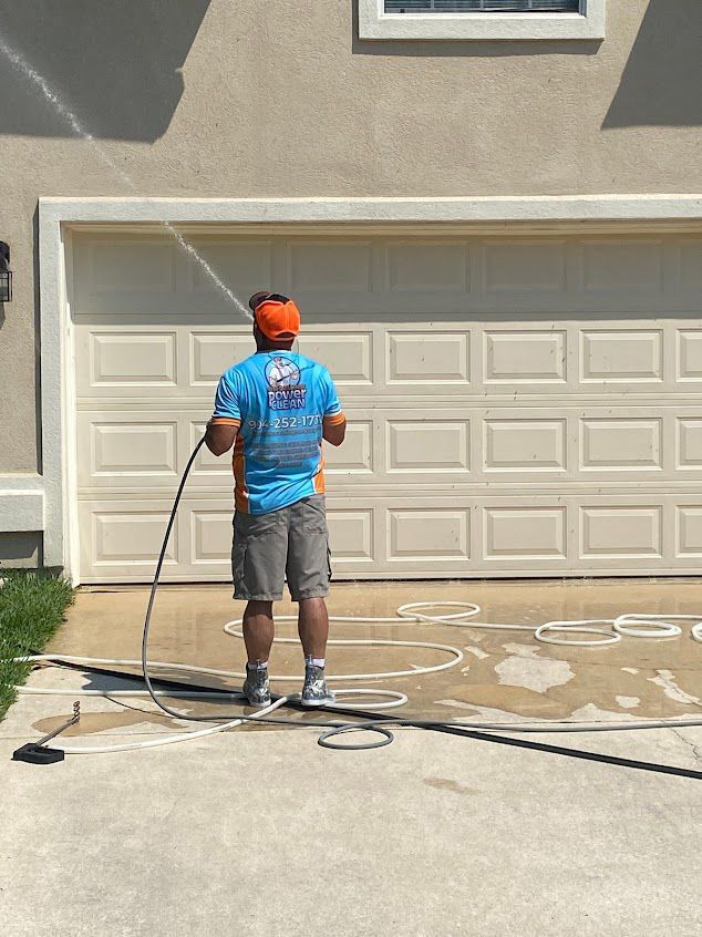 Person power washing a garage door and driveway; beige and tan colors.