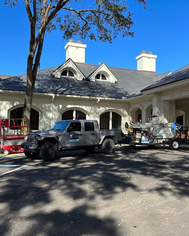Jeep truck pulling a trailer in front of a light-colored building with dark gray roof, blue sky.