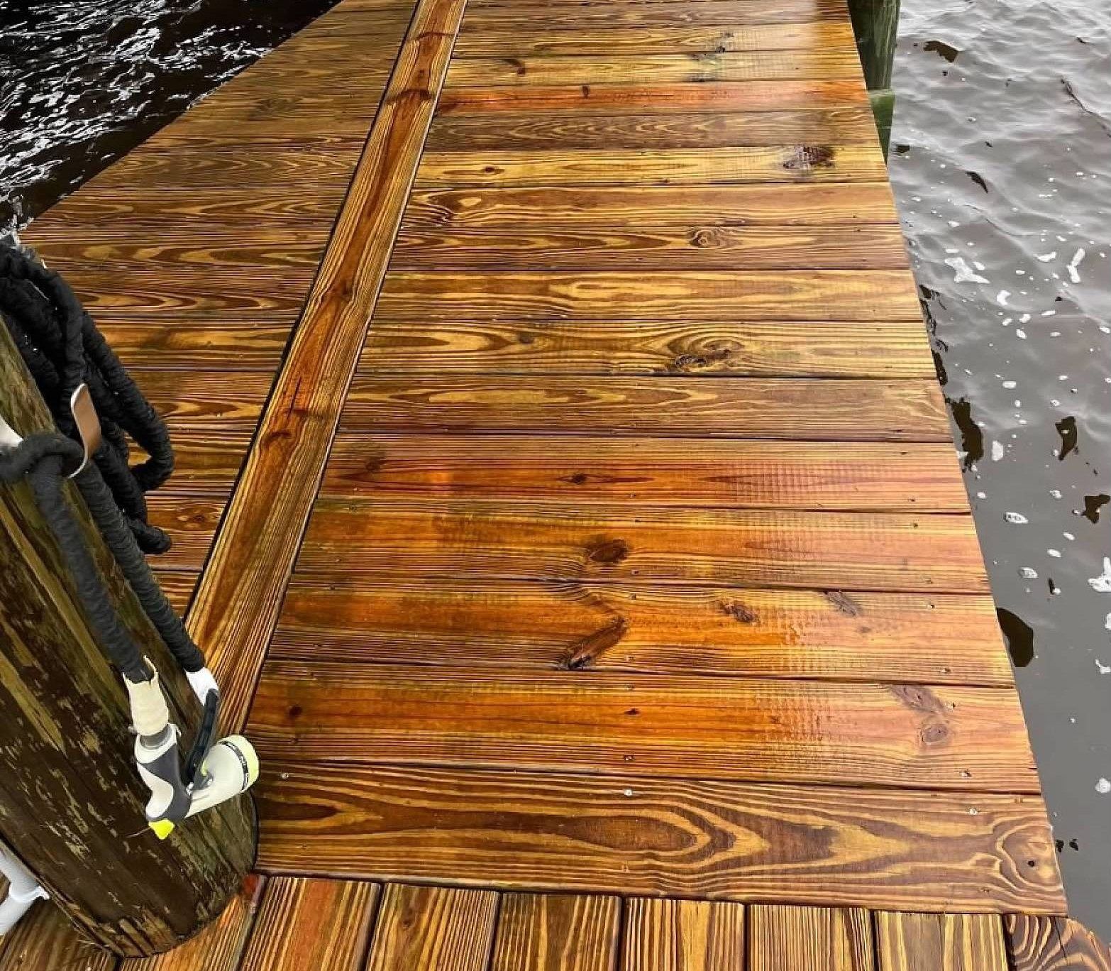 Wooden dock planks next to water. The wood has a brown stain and shows wood grain. A rope is attached.