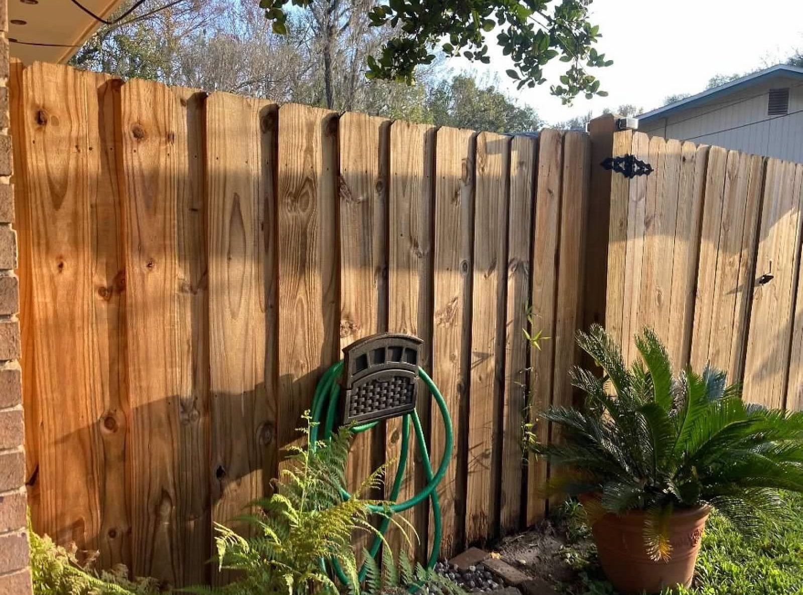 Wooden fence with a mounted hose and a potted plant in a sunny outdoor setting.