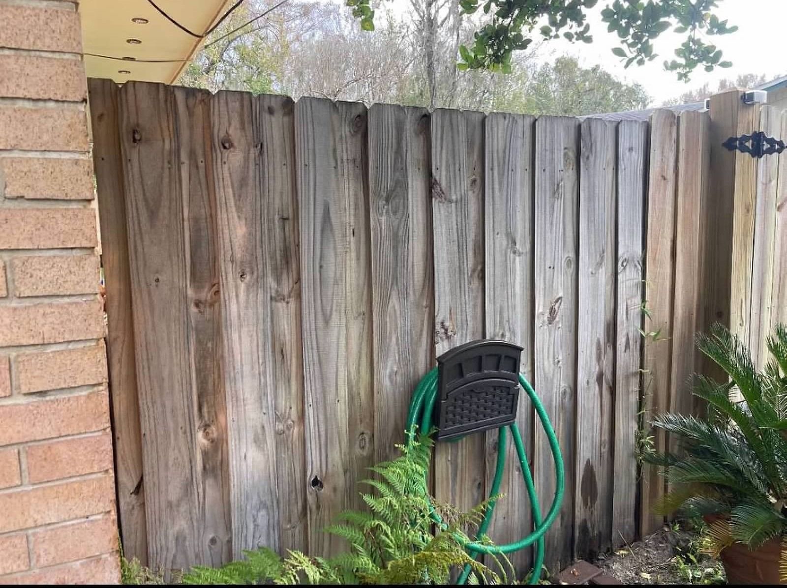 Wooden fence with attached hose and holder next to a brick wall.