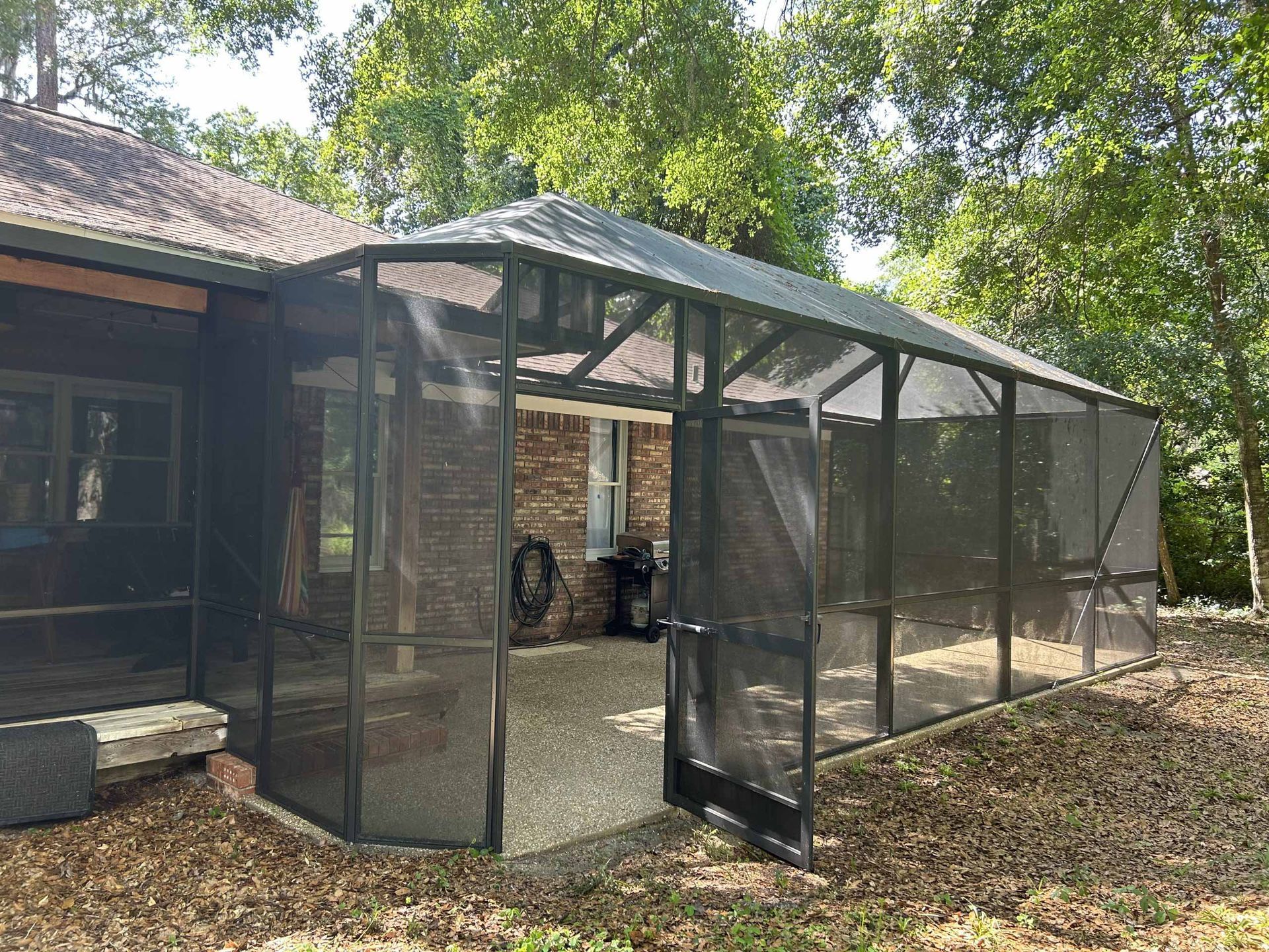 A screened-in porch attached to a dark-colored house, with gravel flooring and an open doorway.