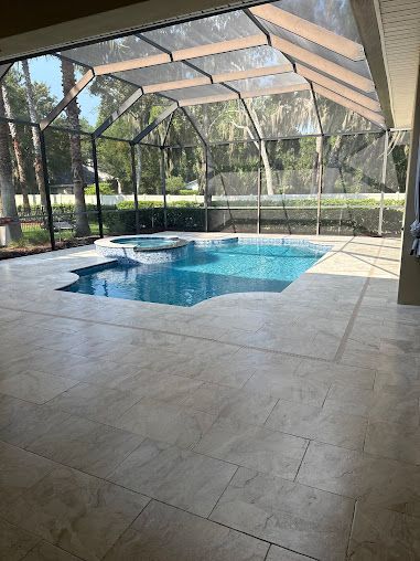 Pool area with screened enclosure and tiled patio. Pool is blue. Sunny outdoor setting.
