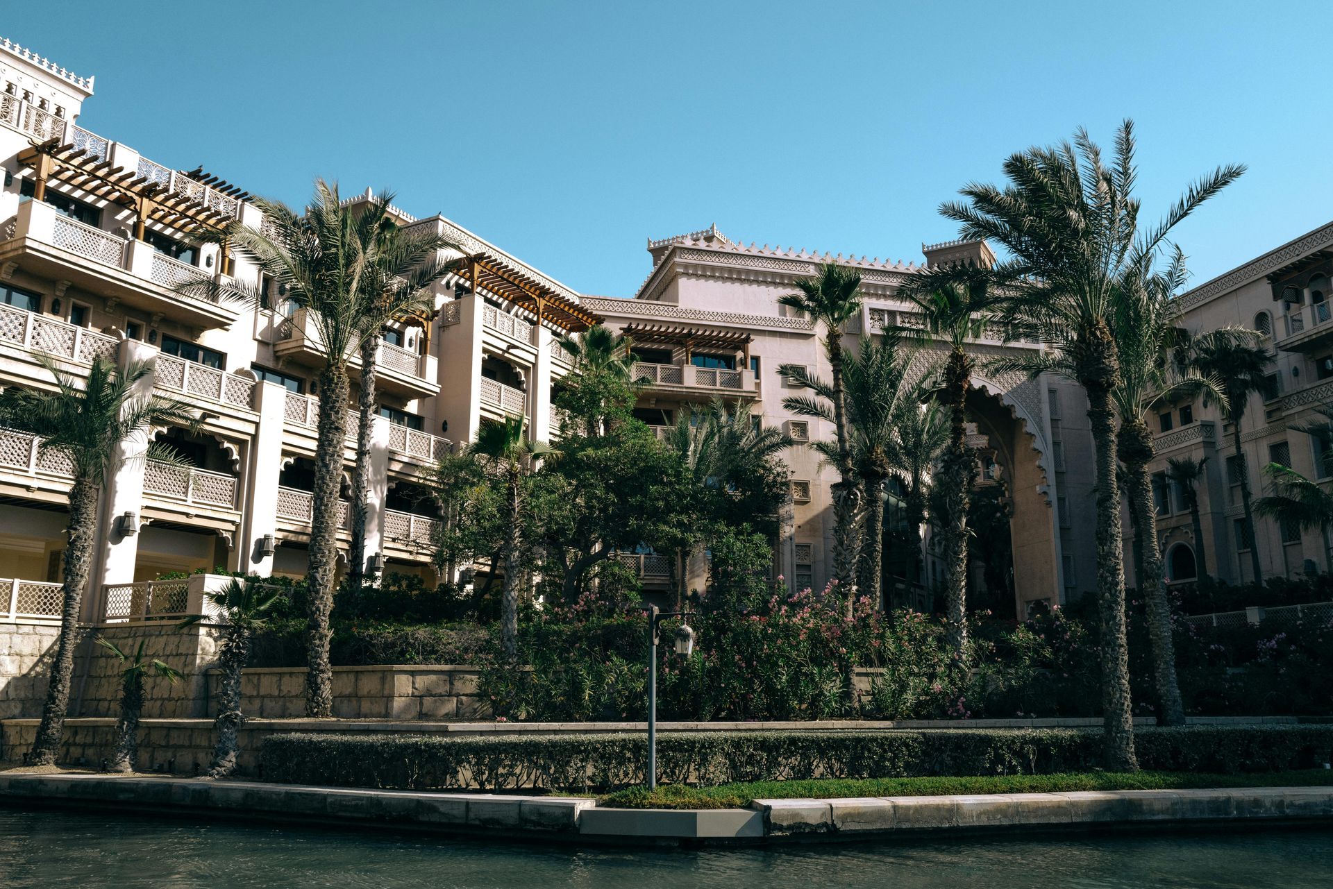 Resort buildings with balconies and palm trees against a clear blue sky.