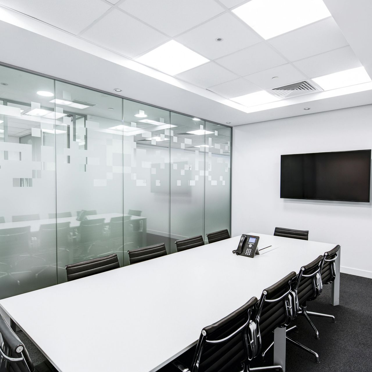 Conference room with long white table, black chairs, glass walls, and large screen.