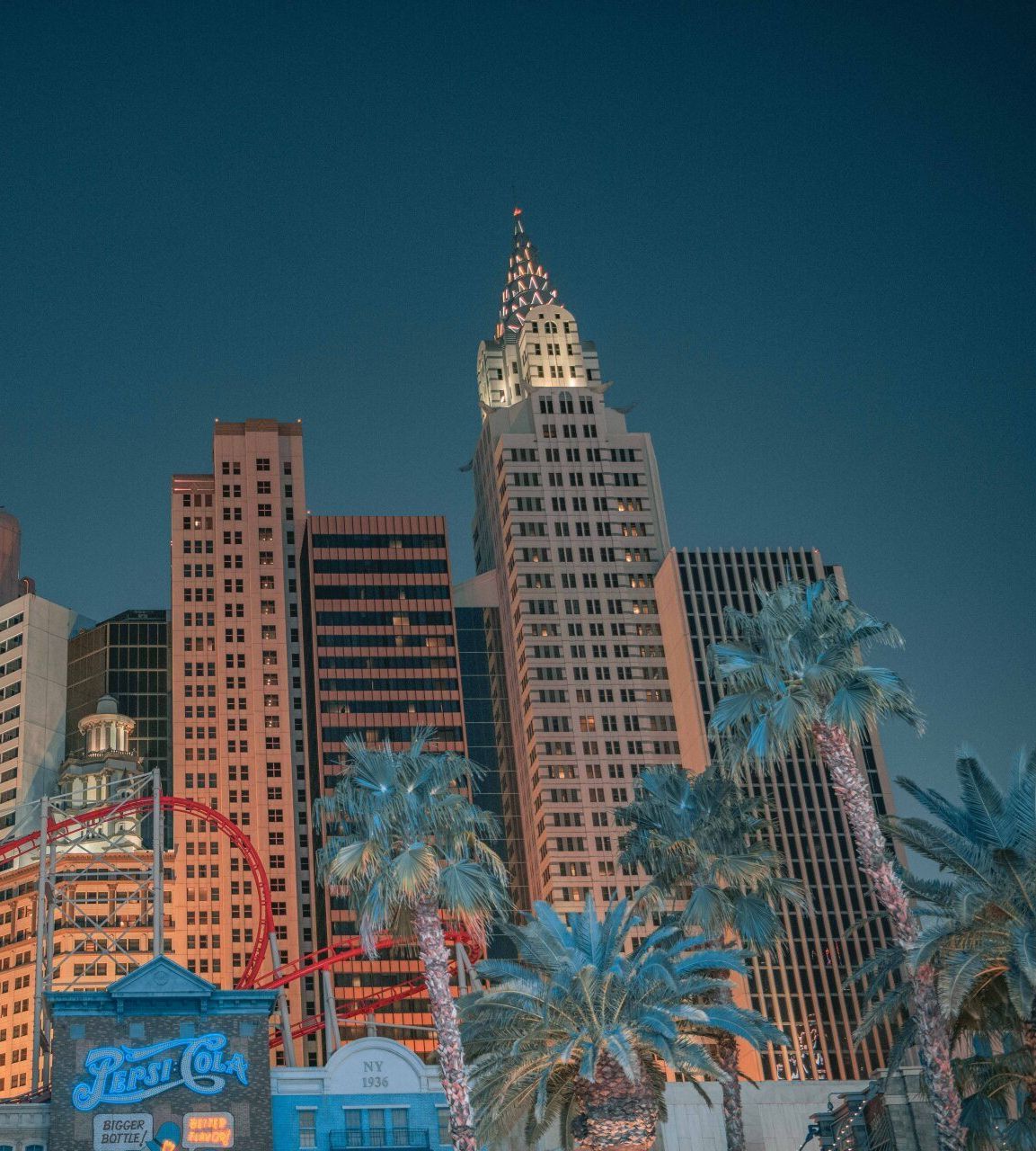 Buildings and palm trees against a blue sky, possibly New York-themed resort in Las Vegas.