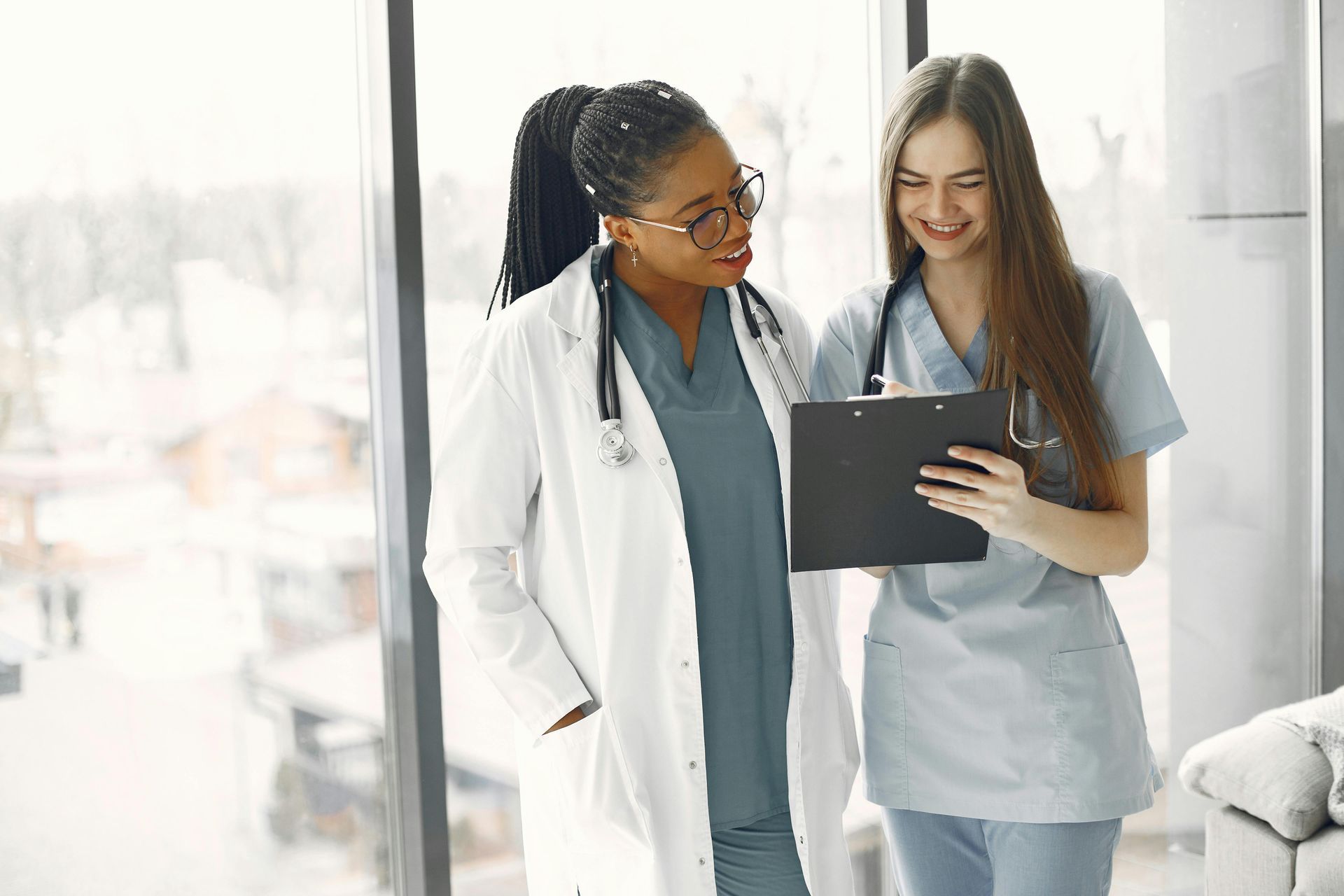 Two medical professionals reviewing documents. One in white coat, one in scrubs, both smiling.