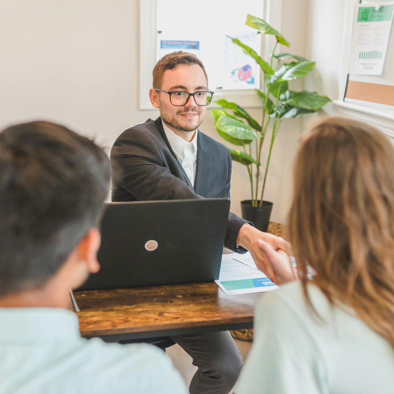 Financial advisor shakes hands with a person, couple in consultation, laptop on table.
