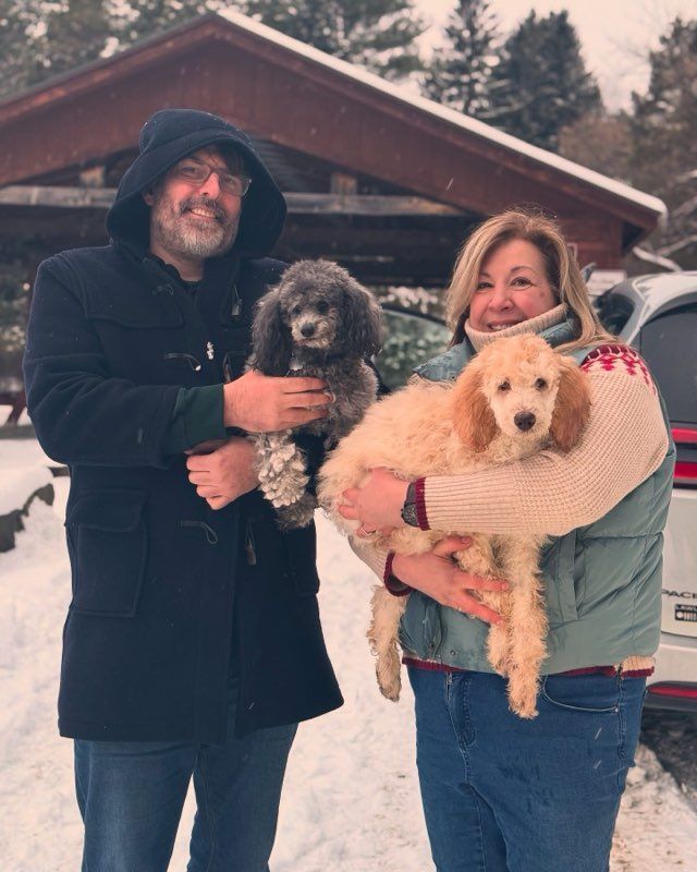 Two people holding their new standard poodle puppies outside