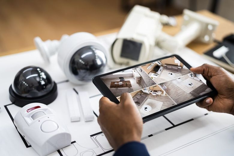 Hands holding a tablet showing security camera feeds beside several white dome cameras on a desk