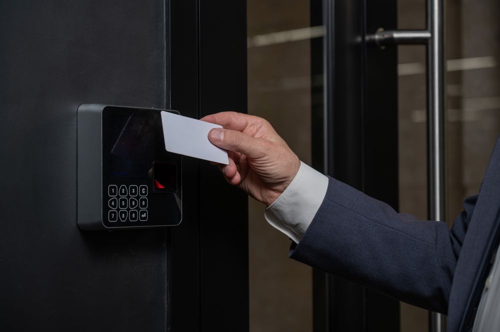 Hand holding a white card to a black card reader on a glass door