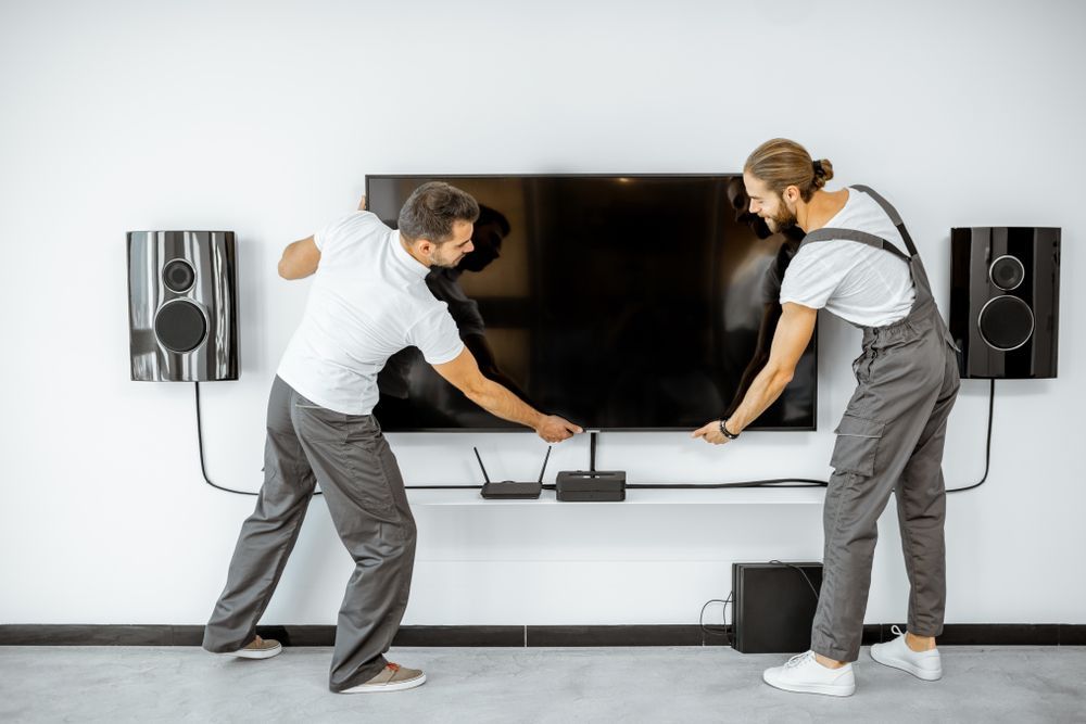Two men mounting a large flat-screen TV on a wall with a soundbar beneath it