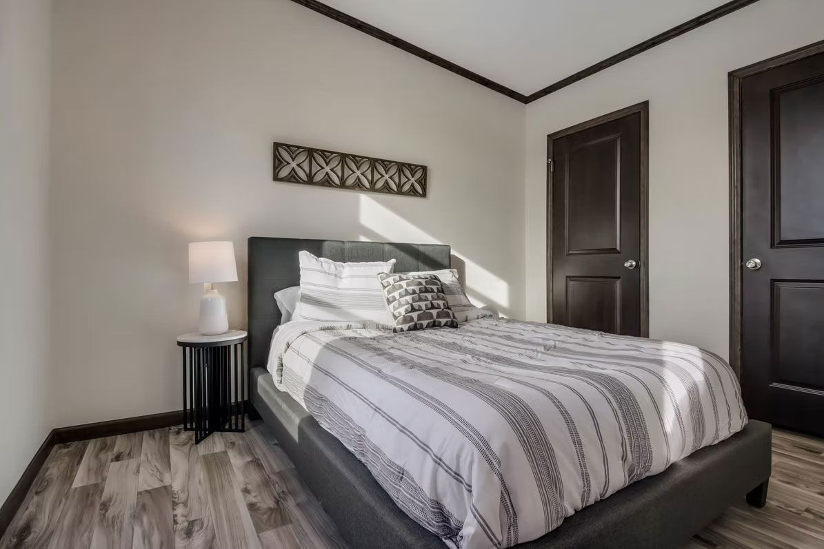 Bedroom with a gray bed, patterned bedding, small side table, and dark brown door.