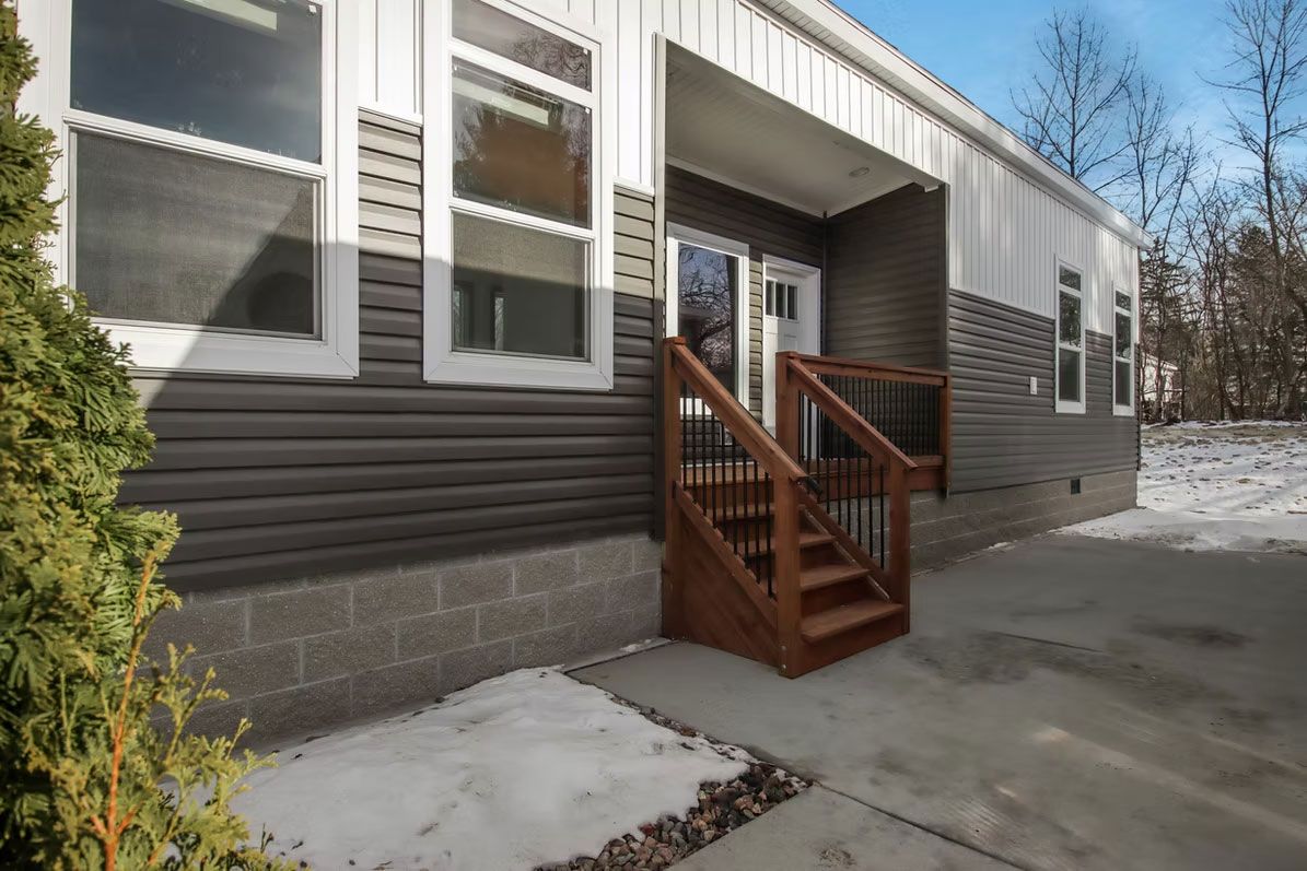 Exterior of a house with a front porch and steps, snow on the ground, siding in shades of gray.