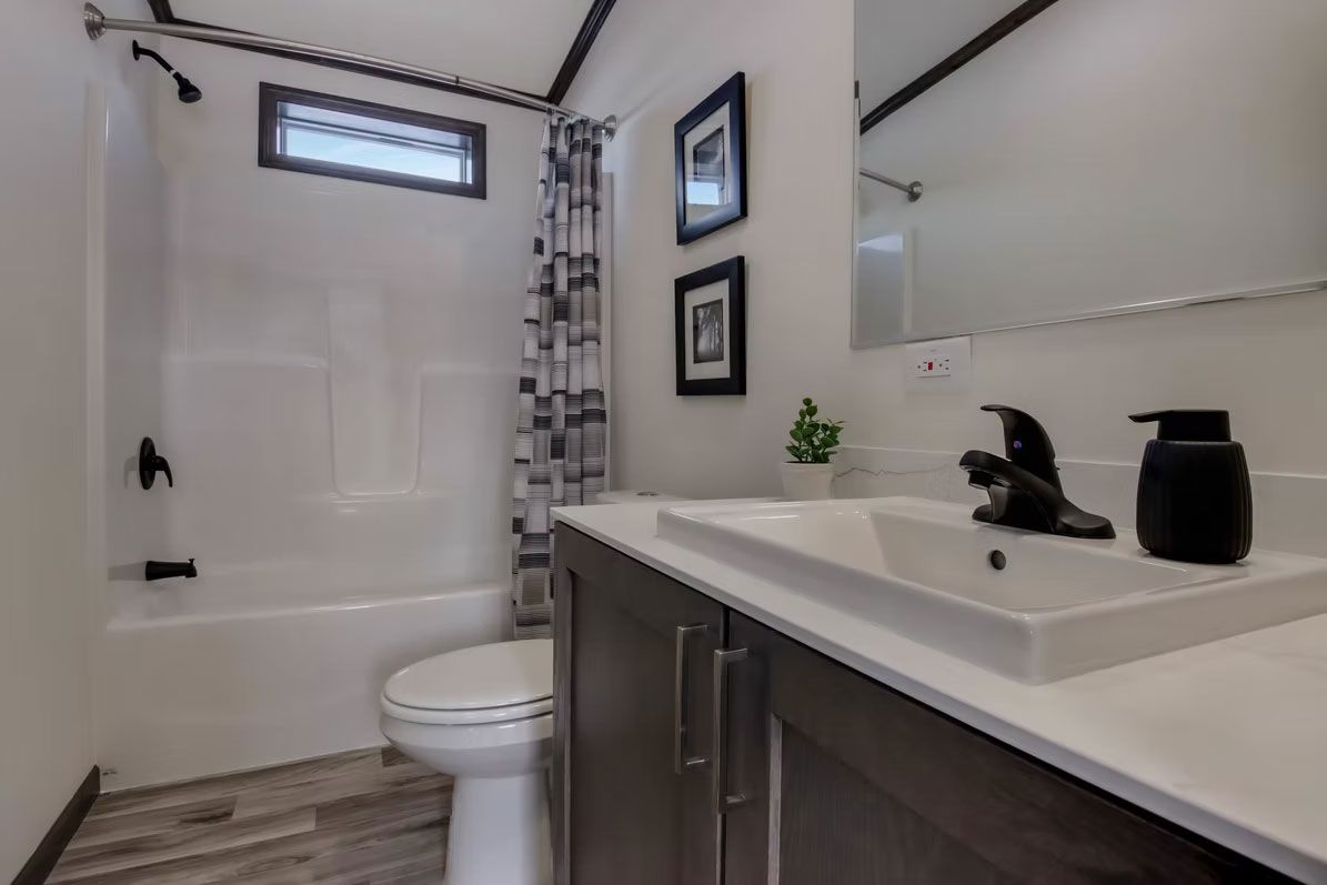 Bathroom with a white sink and countertop, black faucet, and white tub with shower curtain.