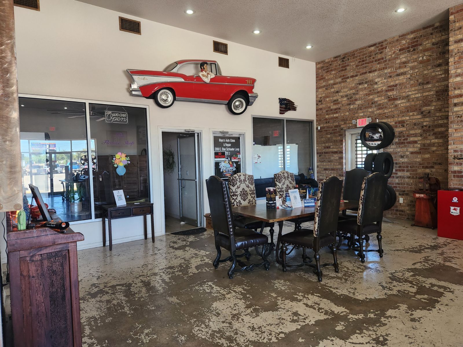 Interior of a car shop waiting area with a red car on the wall, a table, and a brick wall. | Mayo Autoworks 2