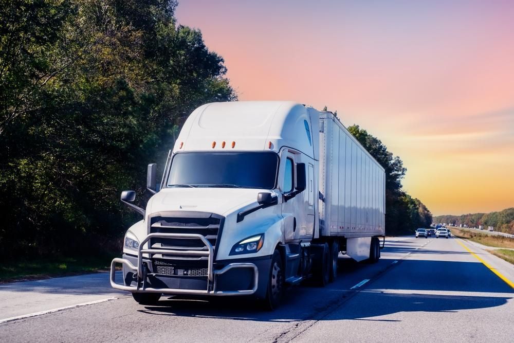 White semi-truck driving on a highway with a sunset background.