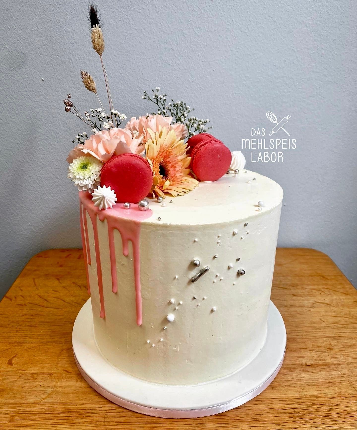 Ein weißer Kuchen mit Blumen und Macarons darauf