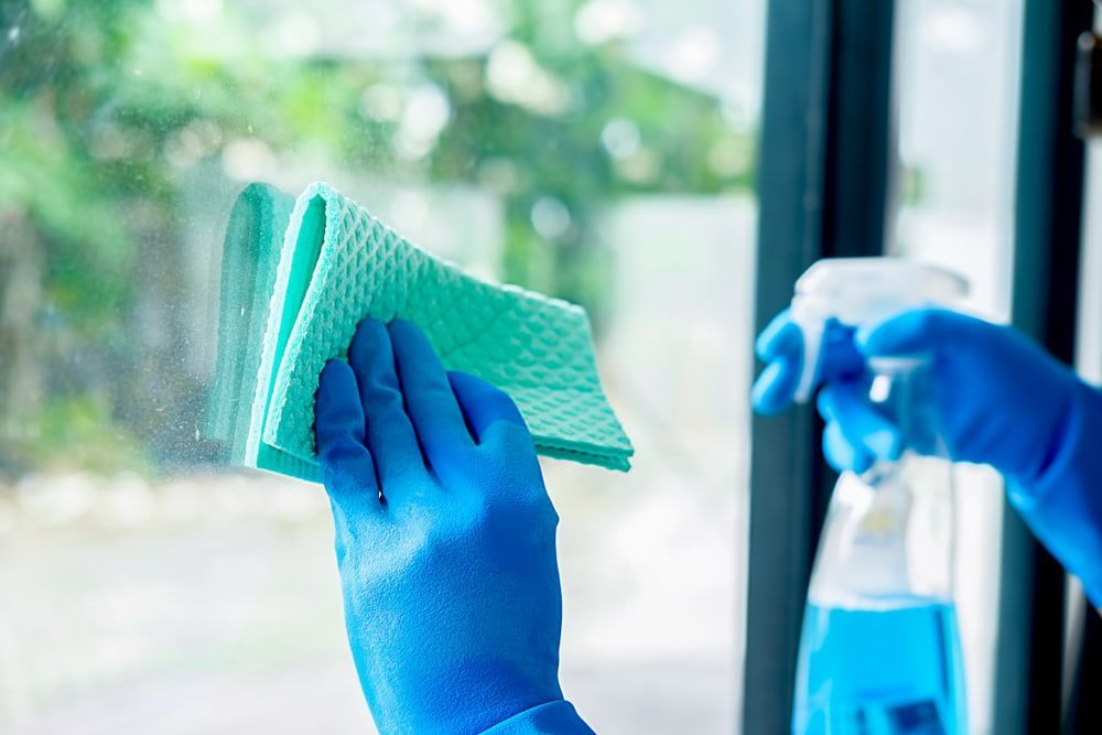 A Person Wearing Blue Gloves Is Cleaning a Window — Complete Clean Home Cleaning in Shellharbour, NSW