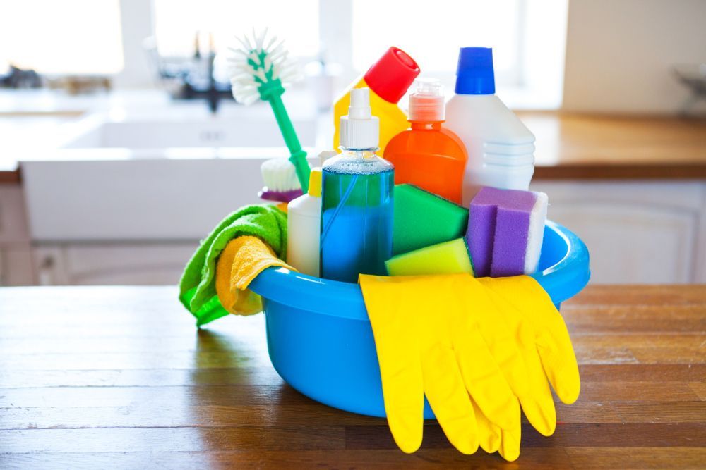 A Blue Bowl Filled With Cleaning Supplies on a Wooden Table — Complete Clean Home Cleaning in Woonona, NSW